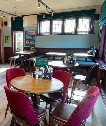An interior restaurant seating area at the Golden Hind, with two dartboards, and upholstered chairs and bench seating.