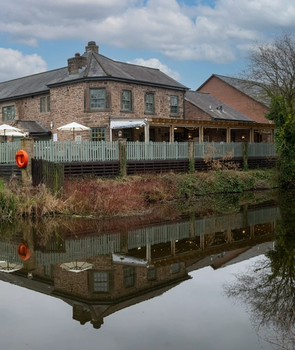 The exterior facade of The Malthouse Farm in Whittle-Le-Woods, with a view of the waterside beside the building.