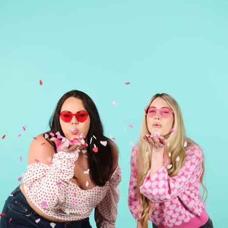 Two women blowing pink confetti