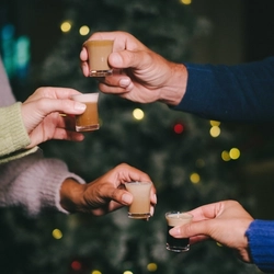 A close up image of 4 shot glasses being held while celebrating with a cheers within the interior of a Greene King venue.