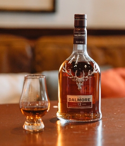 A bottle of The Dalmore Whisky on a table next to a whisky glass.