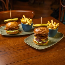 A Chicken Burger and a Pulled Pork Beef Burger, each served on a plate with a bowl of fries, sitting on a wooden restaurant table.