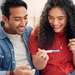 A stock image of a couple holding a pregnancy test and smiling.