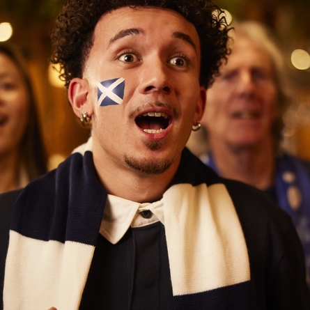 An image of a man wearing a sport team scarf, watching a sporting event.