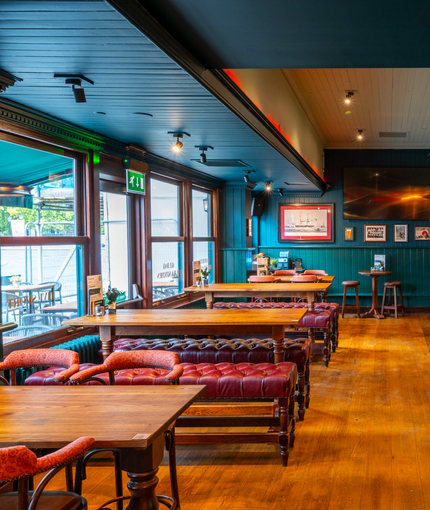 An interior restaurant seating area of the Scholars Arms; with upholstered bench seating, a TV on the wall, and a Shufl table.