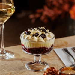 An advertising image of a Trifle dessert and a glass of white wine within the interior restaurant seating area at The Foundry Bell.