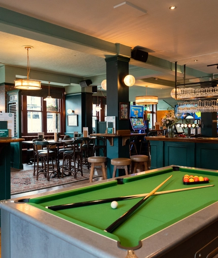 The bar and interior restaurant seating area at The Richmond Arms, with a pool table, bar stool seating, and gaming machines.
