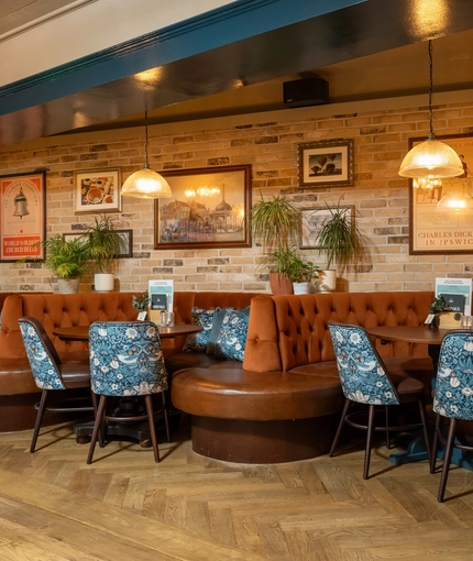 The interior restaurant seating area of the Cock & Pye, with upholstered booth seating and framed artwork on the wall.