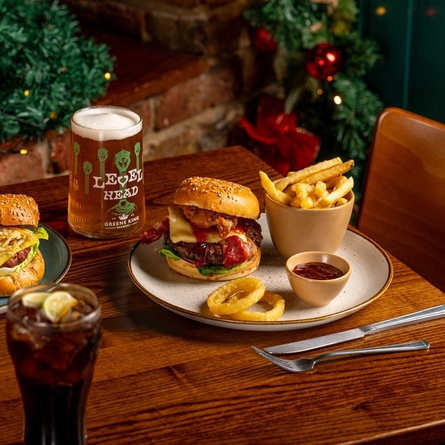 Two burgers, served with fries, onion rings and sauce, next to a pint of Level Head on a table.