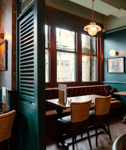 An interior restaurant seating area at The Richmond Arms, with wooden flooring, and an upholstered booth seat against the windows.