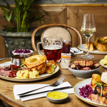 Plates of food and drinks sitting on a wooden table of a pub