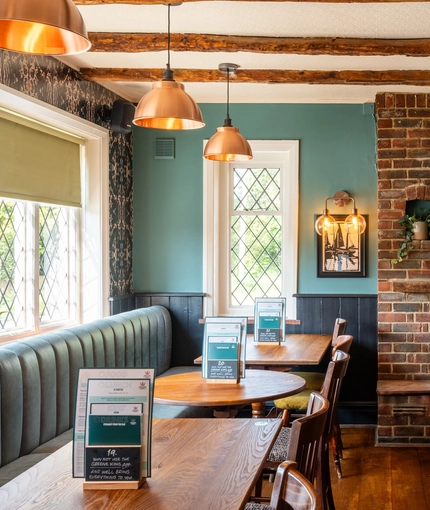 An interior restaurant seating area at The Walkford, with an upholstered booth seat in front of the leaded windows, wooden beams on the ceiling, and a brick fireplace.