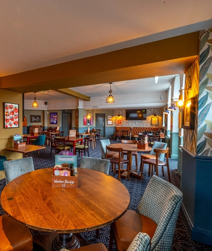 The interior restaurant seating area at the Wooden Bridge in Guildford, with upholstered chairs, and a TV on the wall.