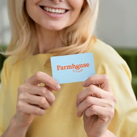 A woman in a yellow t-shirt holding a light blue Farmhouse Kitchens gift card while smiling.