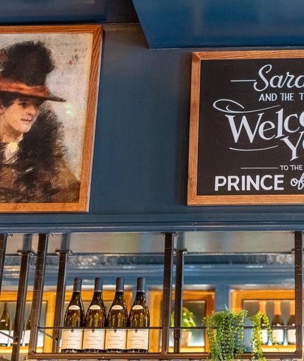 A sign on the wall that says 'Sarah and the team welcome you to the Prince Of Wales'.