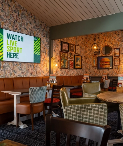 The interior restaurant seating area of The Man On The Moon, with wooden tables, upholstered booth seating, and TVs and framed artwork on the walls.
