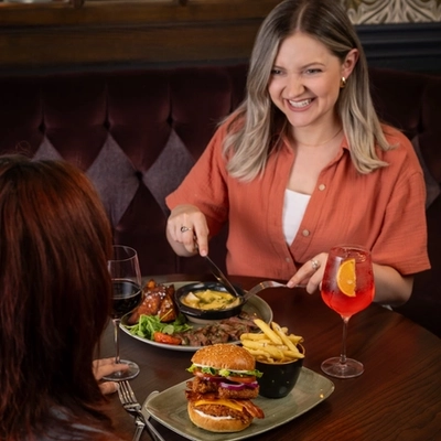 Two friends seated at the restaurant area in a Greene King Community Pubs with Food venue enjoying mains off the specials menu.