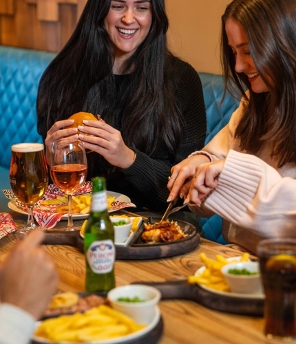 An image showing a group of people sat around a table enjoying mains dishes and drinks at a Flaming Grill venue.