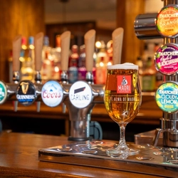 A close up view of the beer taps on the bar inside The Parsonage, with a glass of beer sitting on the counter.