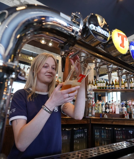 A woman pours a pint of beer from the beer taps at Shakespeares in Edinburgh.