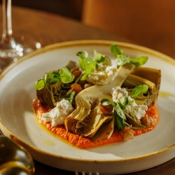 An advertising image of a Small Plates dish consisting of vegetables, cheese and sauce within the interior restaurant seating area at The Foundry Bell.