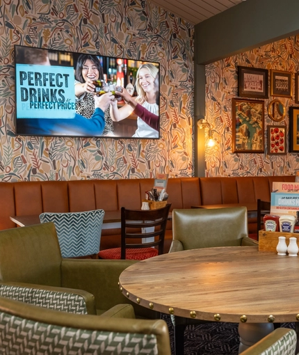 The interior restaurant seating area at The Man On The Moon, with wooden tables, upholstered seating, and TVs and framed artwork on the walls.