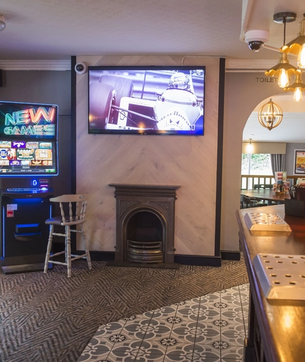 Interior bar of a pub with a seating area, a TV, a gambling machine and a fireplace.