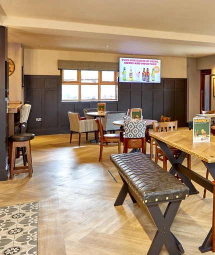 The interior restaurant seating area of The Flying Horse in Heald Green, with wooden tables, upholstered chairs, TVs on the walls and a gaming machine.