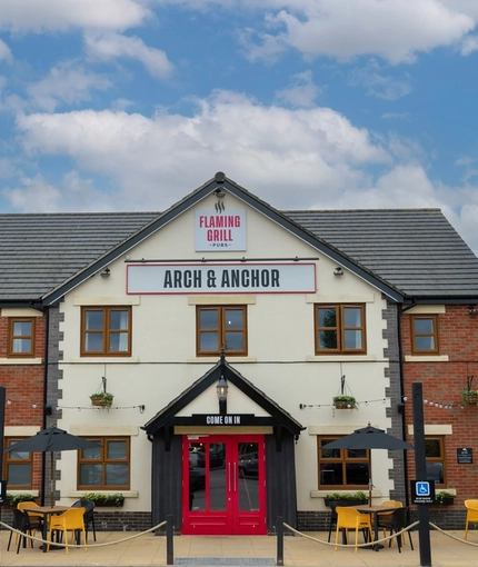 The exterior facade, signage, car park and beer garden seating area of the Arch & Anchor in Widnes.