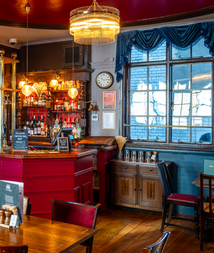 The interior restaurant seating area and small bar at the Two Chairmen, with wooden flooring, and framed artwork on the wall.
