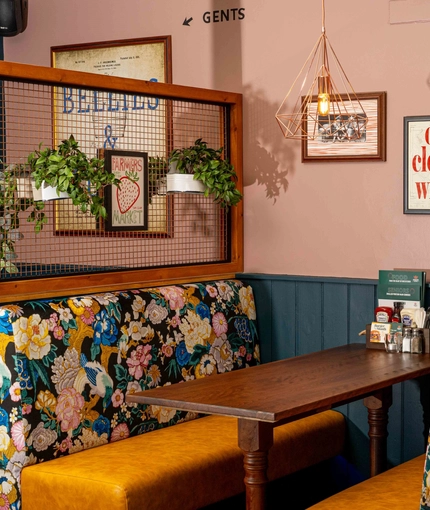 An interior restaurant booth seating area at The White Hart, with upholstered seats, framed artwork on the walls, and potted plants above the seats.