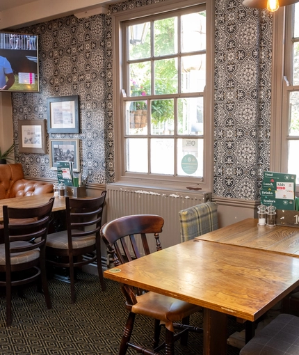 An interior restaurant seating area at The Woolpack Inn; with an upholstered booth seat against one of the windows, and a large TV on the wall above it.