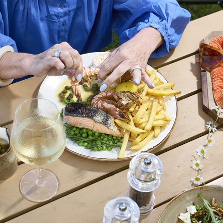 A lifestyle image showing a person sat at a table enjoying a Seafood Platter dish and a glass of white wine within the exterior beer garden seating area at a Chef & Brewer venue.