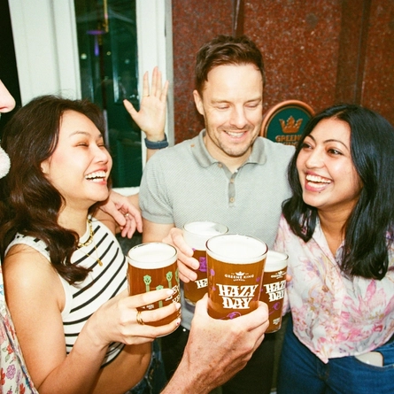 A group of friends stood outside a Greene King venue in London in the seating area with drinks being held in a 'cheers' position.