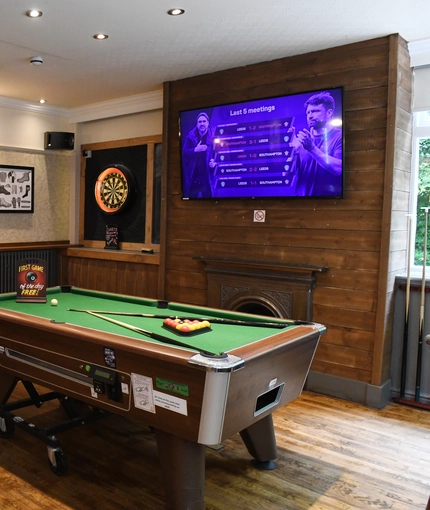 Interior dining area of a pub with a TV, a pool table and a dartboard.