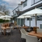 The exterior facade, signage, and seating area of The Hollybush, with shade umbrellas on some of the wooden tables, and flower baskets hanging from the veranda.