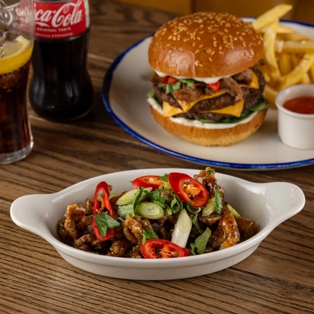 A roasting dish containing Crispy Chilli Beef on a wooden table.