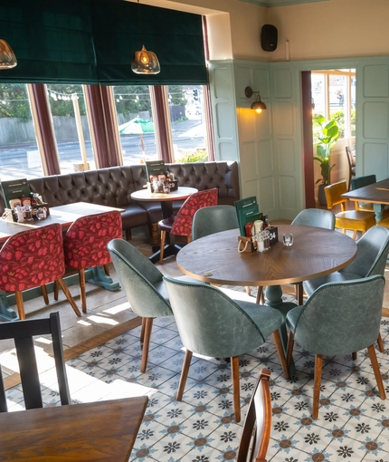 The interior restaurant seating area at the Golden Hind in Cambridge, with tiled flooring, wood panelled walls, and upholstered chairs and window seat.