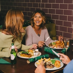 An image of a group of friends sat at a table enjoying Xmas Day main dishes and various drinks within the interior restaurant seating area at a Pub & Carvery venue.