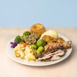 A Carvery dinner featuring slices of roast meat, Yorkshire pudding, mashed potatoes, roast potatoes, Brussels sprouts, broccoli, carrots, cauliflower cheese, pigs in blankets and stuffing, served on a plate.