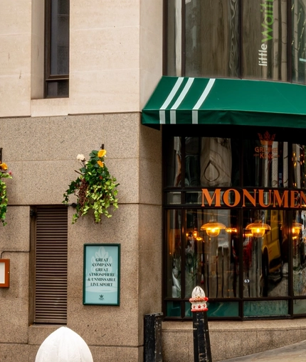 The exterior facade, signage and seating area of the Monument in Whitechapel.