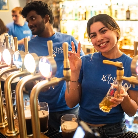 An image of a member of staff stood behind the interior bar pulling a pint of lager at The Kings Stores.