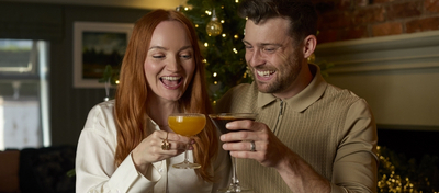A banner showing 2 people holding cocktails and celebrating with a cheers with plated picky bits sat on the table to advertise Christmas at Chef & Brewer.