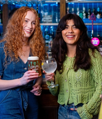 Two women holding a glass of Level Head and a glass of Gin next to the bar.