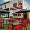 The exterior facade, signage, and beer garden seating area at The Cherry Tree; with shade umbrellas on some of the tables, and string lights overhead.