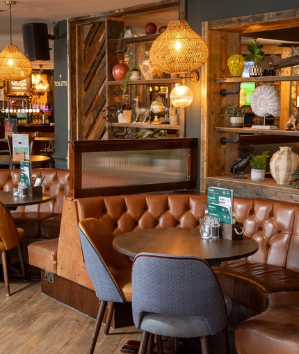 An interior restaurant seating area at the Rudds Arms; with two semi-circular booth seats, and wooden shelves behind them filled with ornaments.