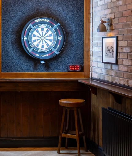 The darts area inside The Railway, with two illuminated dartboards, a small restaurant table, and a pub gaming machine.
