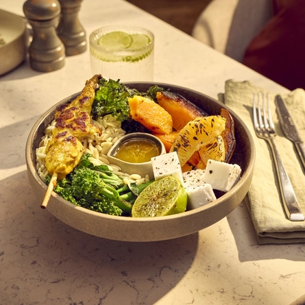 An advertising image of a bowled Warm Orzo Salad with Tandoori Chicken Skewer dish from the Autumn/Winter menu available at The White Horses.