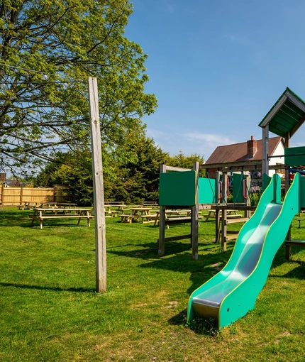 The exterior beer garden seating area and children's play area at The Walkford, with wooden picnic tables, and climbing frame with a slide.