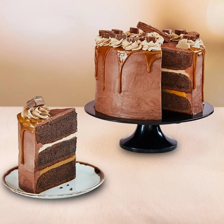 A slice of Marz Attack cake served on a plate which sits on a table. The rest of the cake sits on a cake stand next to the plate.